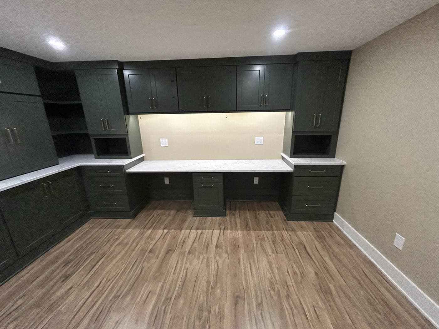 A home office built-in with dark green cabinetry, a marble desk surface, under-cabinet lighting, and recessed cans overhead.