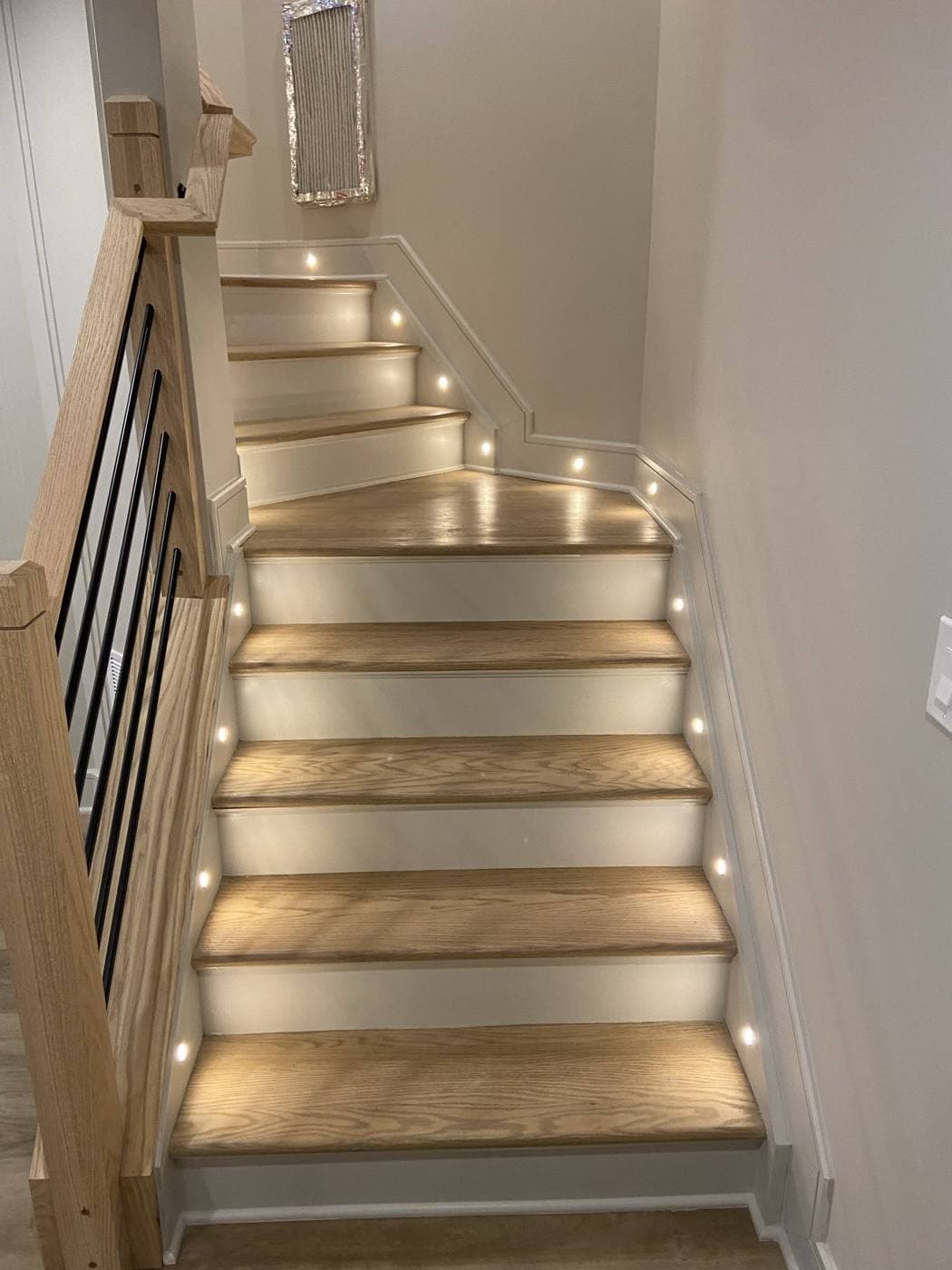 A staircase with oak treads and white risers, with small recessed lights set into the wall at every second tread.